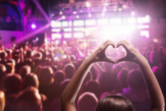 Raised hands. Girl with heart-shape symbol enjoying her favorite group on the concert. Rock concert audience party concept